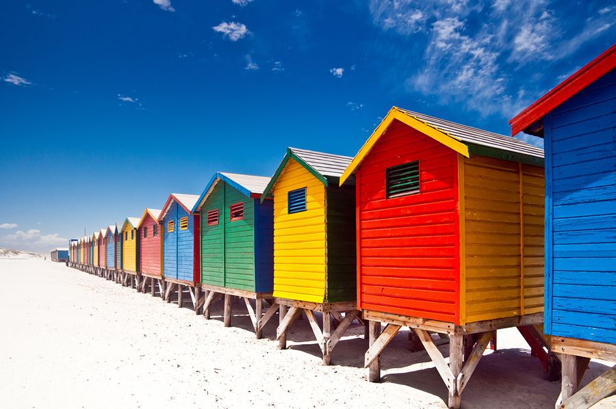A photo of a row of brightly coloured beach huts, taken on a sunny day.