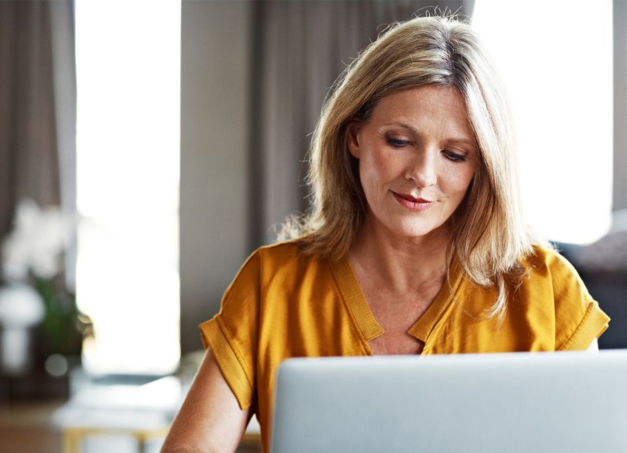 A woman in a yellow shirt sat behind her laptop in her living room.