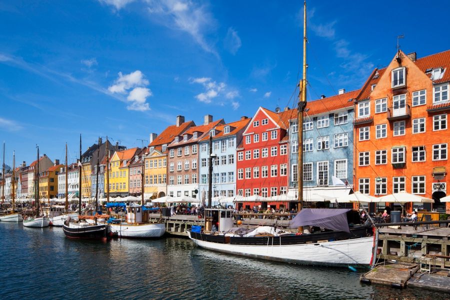 A photo of Copenhagen’s brightly coloured buildings at the port, with small sailing boats moored up on the dock. 