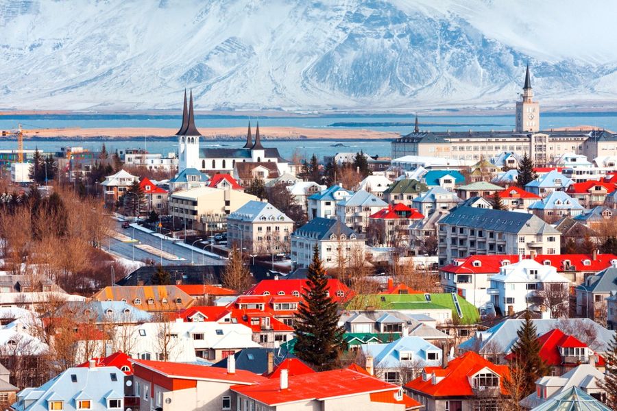 A photo of brightly coloured rooftops in Reykjavik, taken with the water’s edge in the background and a snowy mountain in the distance.
