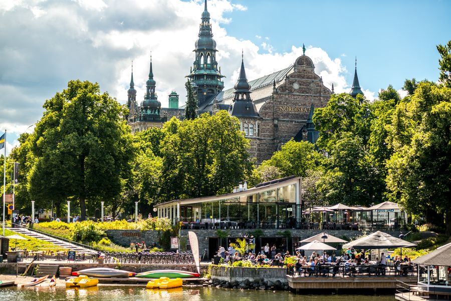 A photo of the Nordiska building in Stockholm, with a café in front, taken by the water’s edge. 