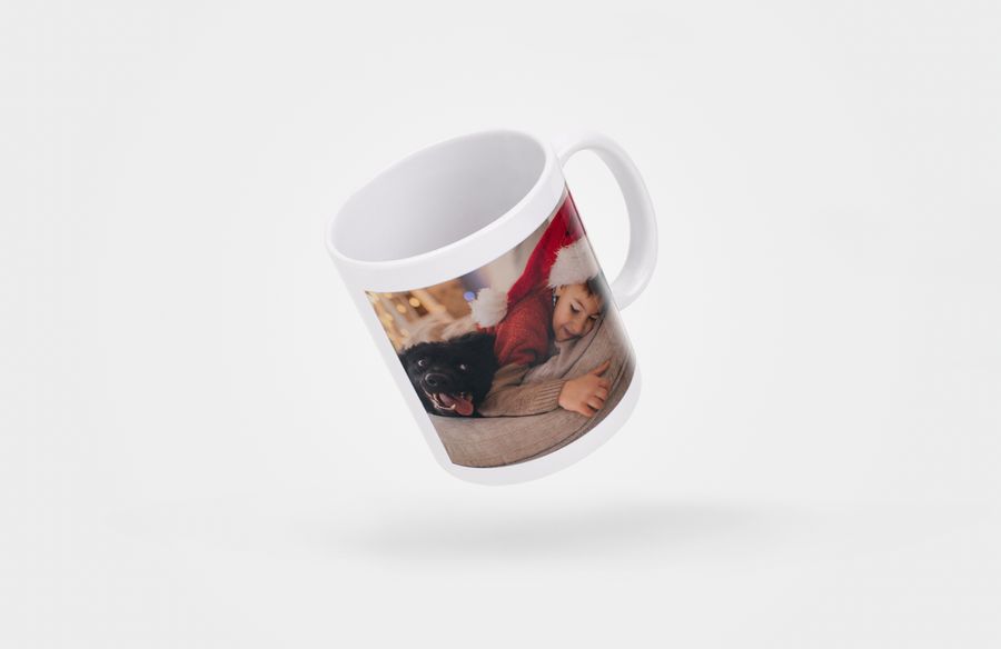 : A photo mug with an image of a little boy in a Santa hat lying on the sofa with his dog