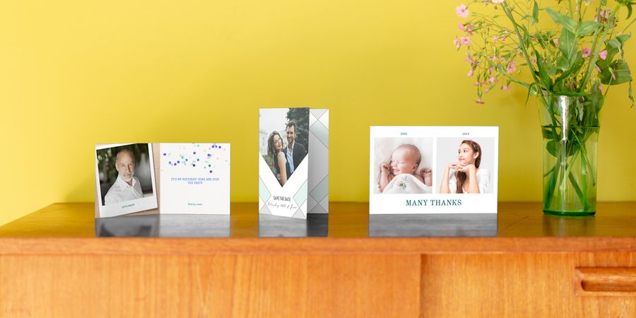 Three personalised photo cards on a wooden side table in front of a yellow wall