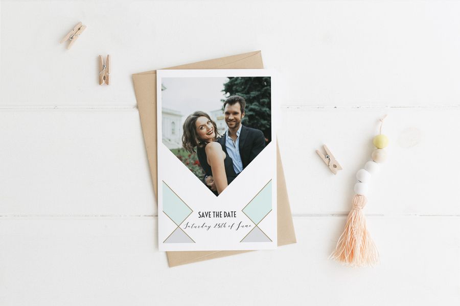A personalised save the date wedding photo card against a white surface with small wooden pegs scattered around