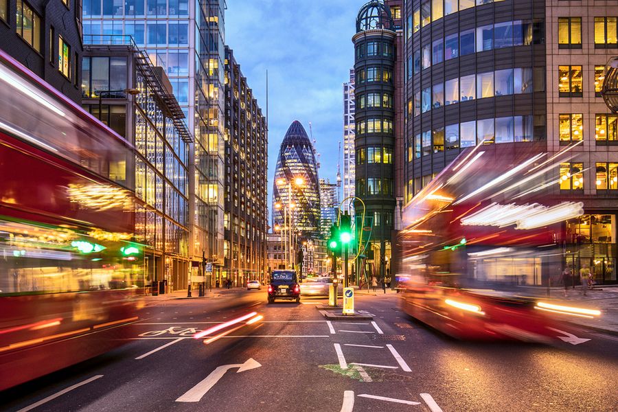 A slow shutter speed-shot of the Gherkin in London, taken at night, with two London buses driving past.