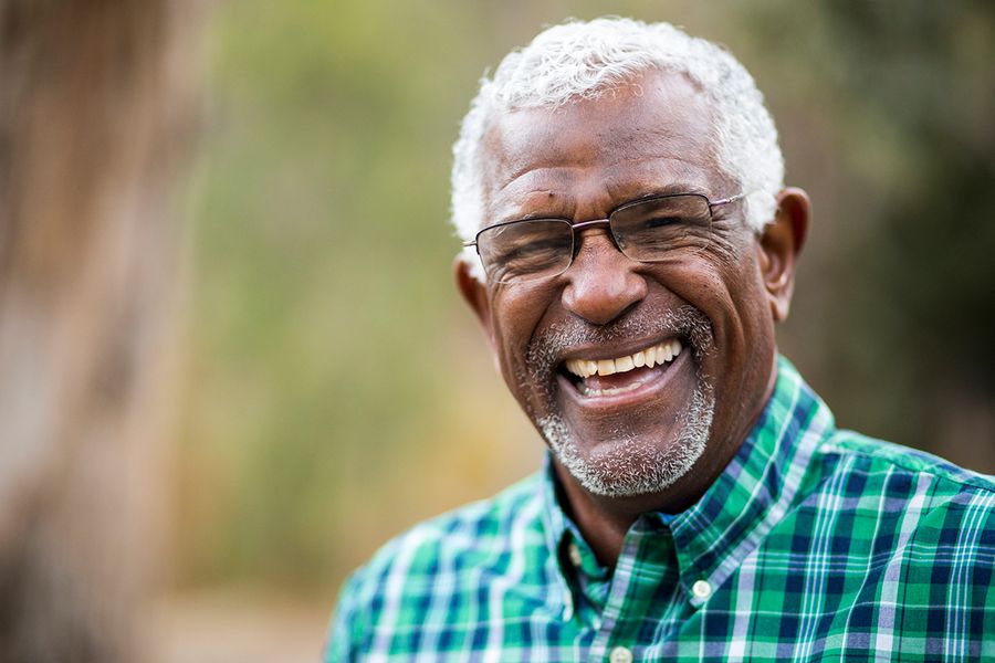 A portrait photo of an older man laughing. There are trees in the background, which are blurry, but the man is in focus.